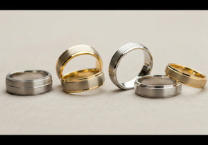 A selection of classic men's wedding rings in different timeless designs and metal types, tastefully arranged on a neutral background.
