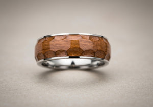 A close-up image of a men's wedding ring with a wood inlay, highlighting the unique wood grain and metallic accents.