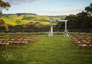 A beautiful outdoor wedding venue set amidst the lush, sunlit hills of Perth with floral decorations and rustic seating.