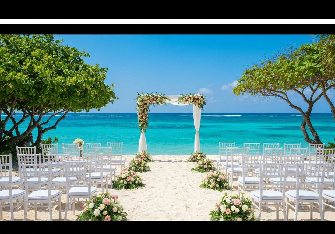 A beautiful beachside destination wedding setup with floral decorated arch, white chairs, and ocean backdrop under a clear blue sky.