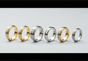 A variety of men's wedding rings in different widths and materials displayed side by side on a simple background.