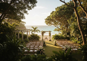 A beautiful outdoor wedding venue in Byron Bay, surrounded by lush greenery, tropical plants, and views of a sandy beach with the ocean in the background.