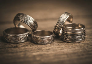 A collection of vintage men's wedding rings with antique designs and intricate details, displayed on a rustic wooden surface.