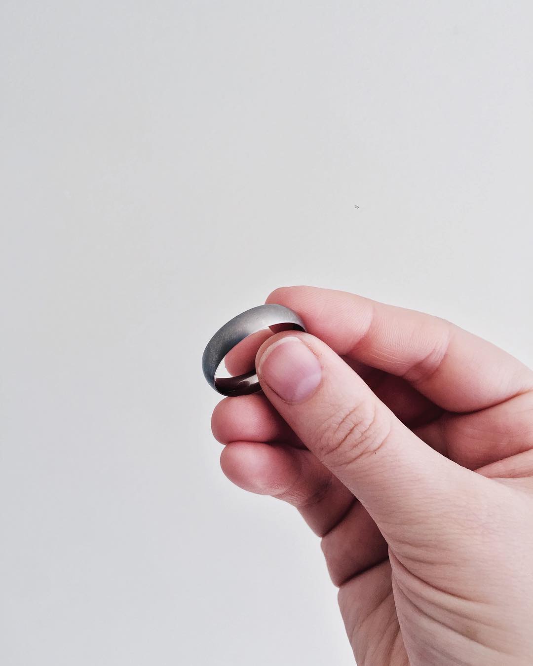 Hand holding a silver ring against a plain background