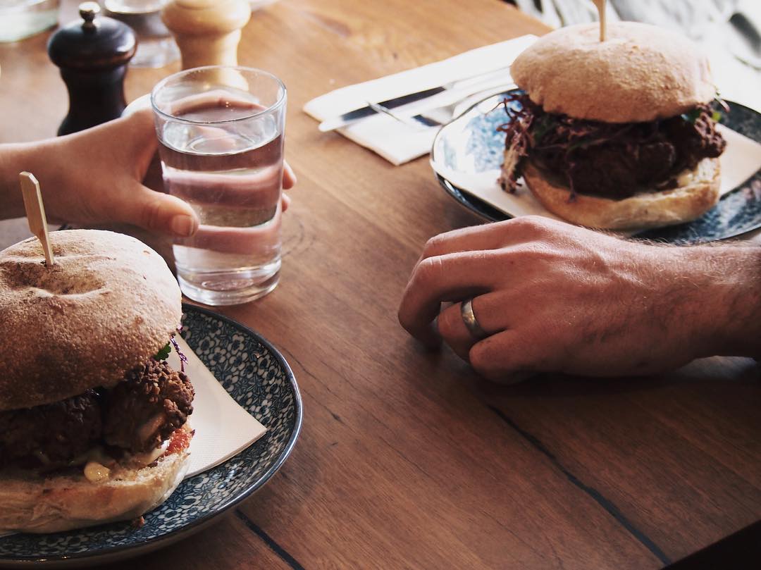 Two people sitting at a table with burgers and drinks
