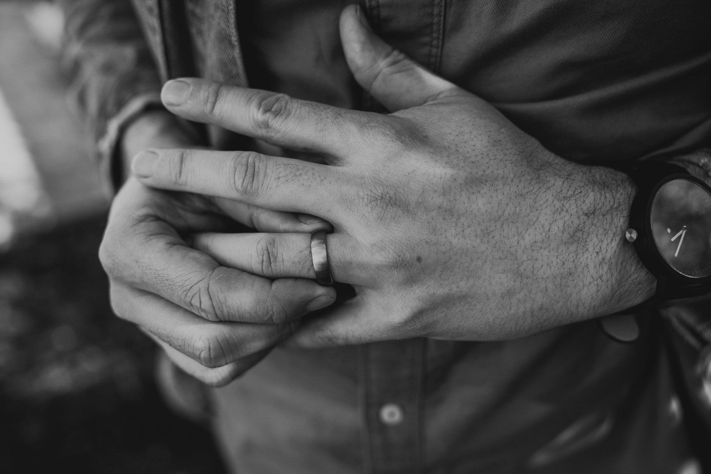 Close-up of a person's hands with a wedding ring, wearing a jacket and watch.
