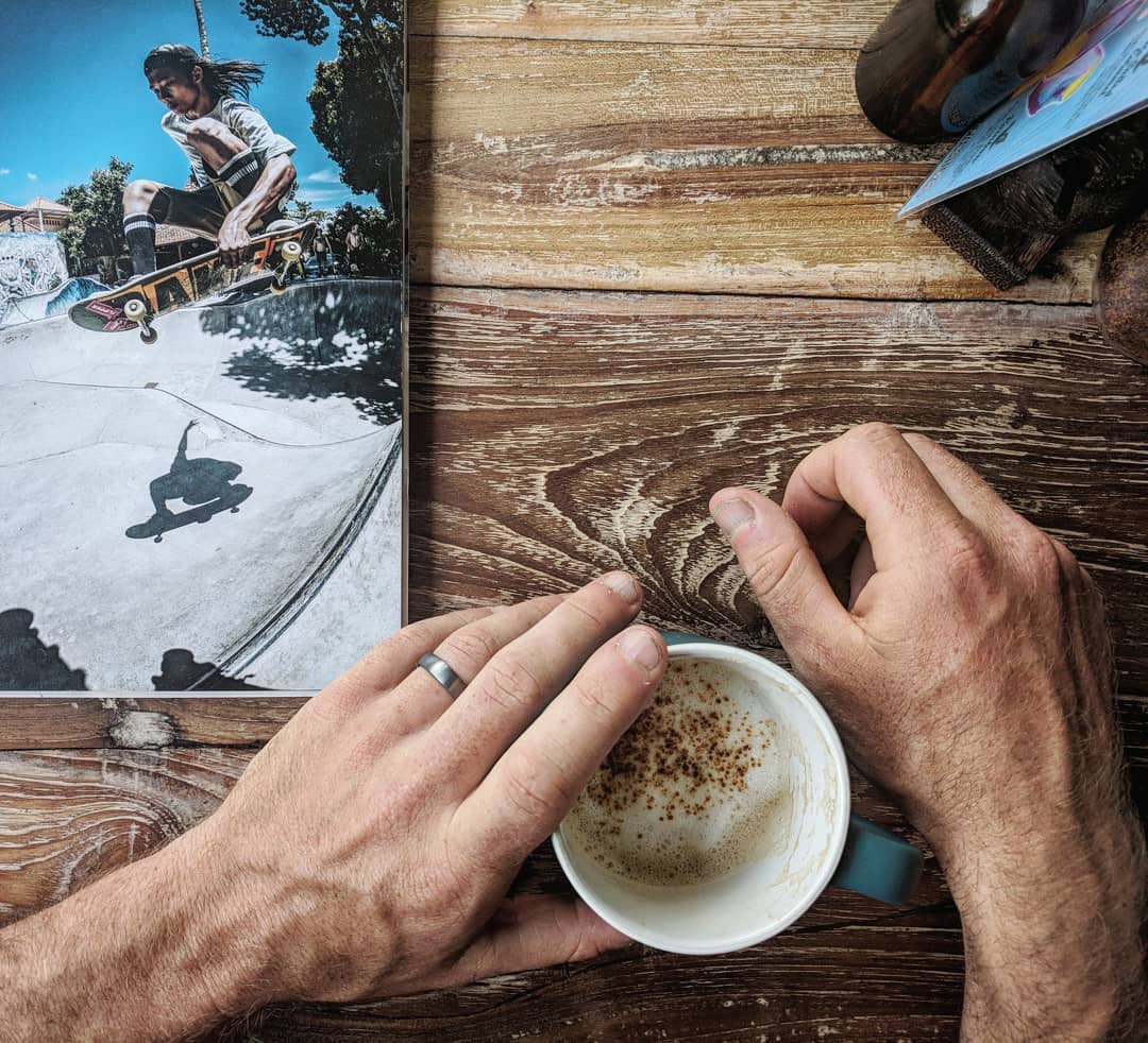 Person holding a coffee cup with a small photo of a skateboarder on a wooden surface.