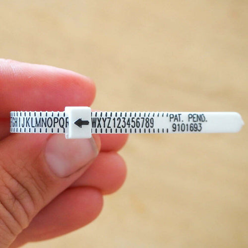 Hand holding a small white ring sizing device with text on a beige background