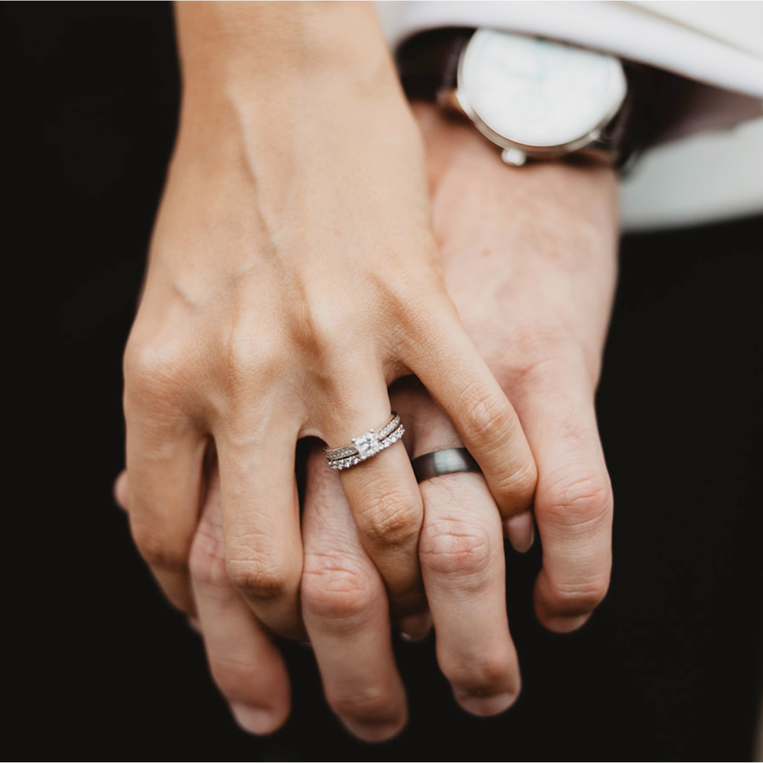 Close-up of two hands holding each other with wedding rings on a dark background