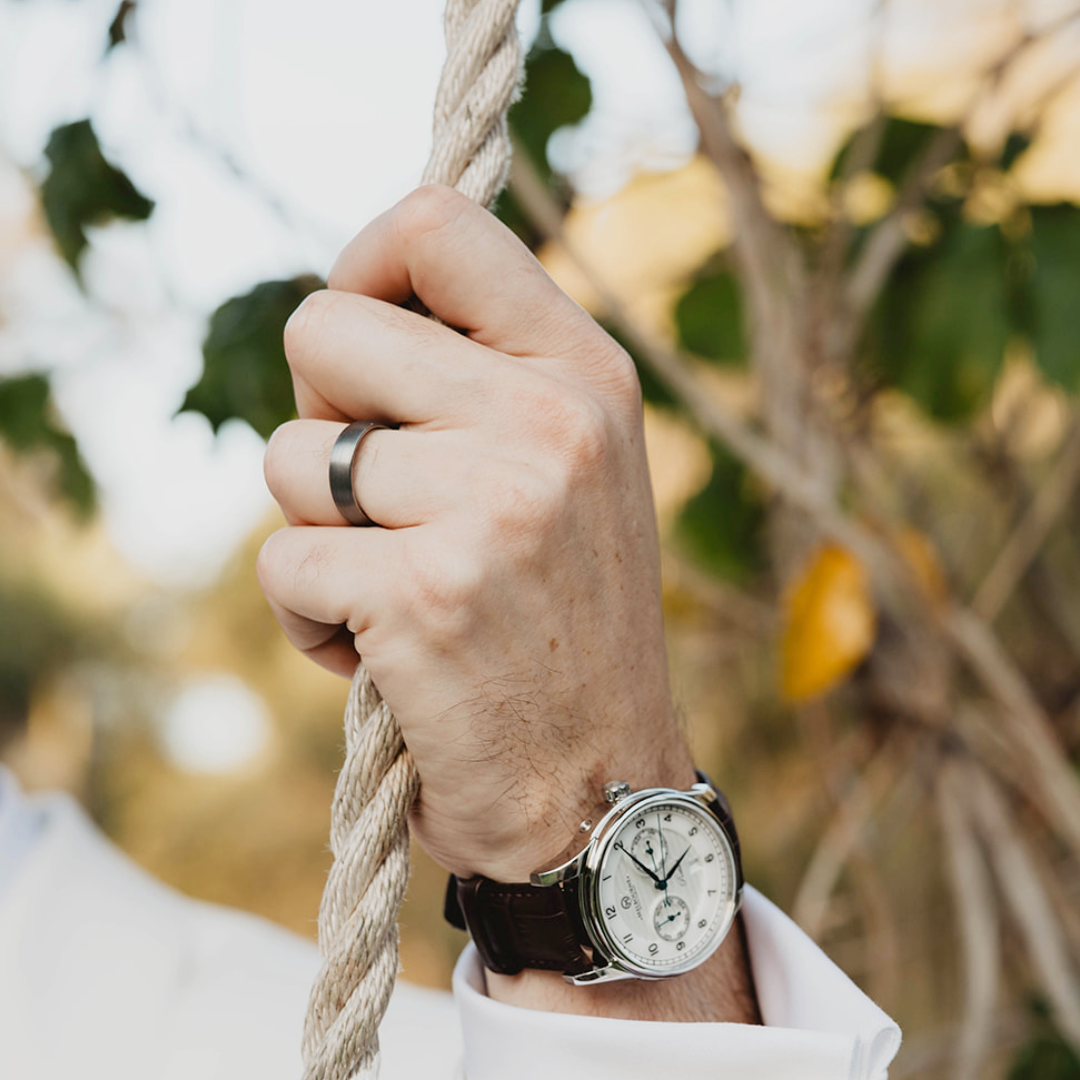 Hand wearing a watch and tungsten wedding ring, holding rope with blurred natural background