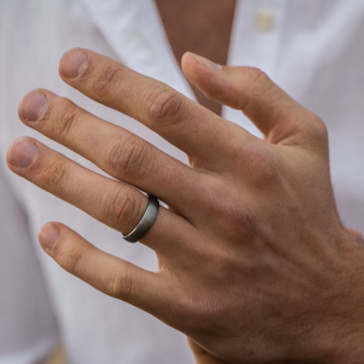 Hand wearing a tungsten wedding ring with a blurred white shirt background