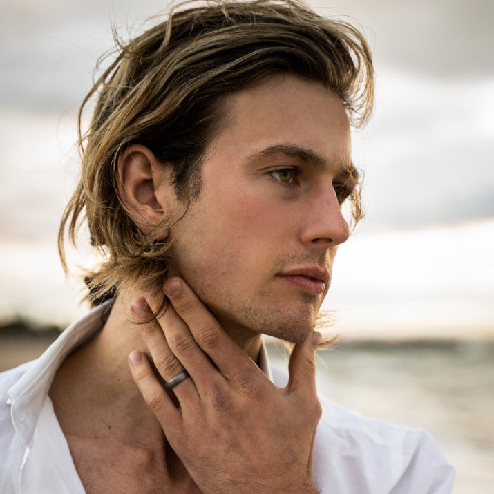 Man with long hair wearing a white shirt and wedding ring, outdoors.