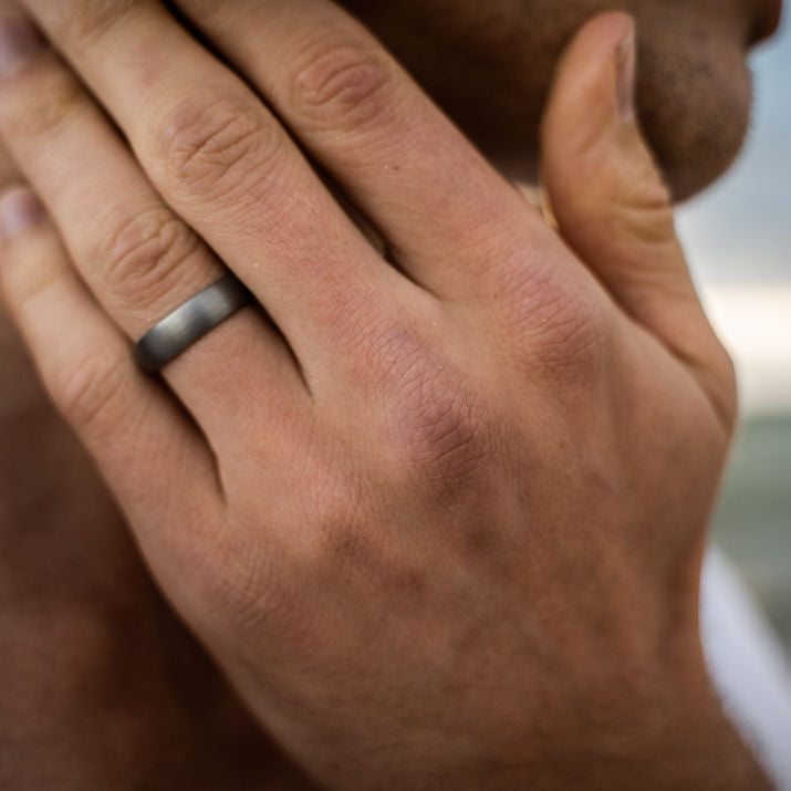 Close-up of a hand wearing a tungsten wedding ring with a blurred background