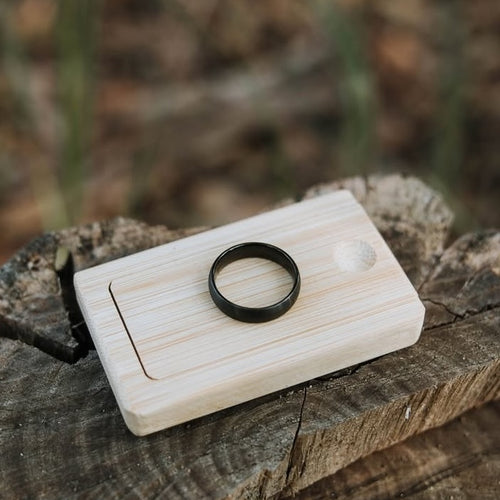 Wooden ring box with a black wedding ring on top.