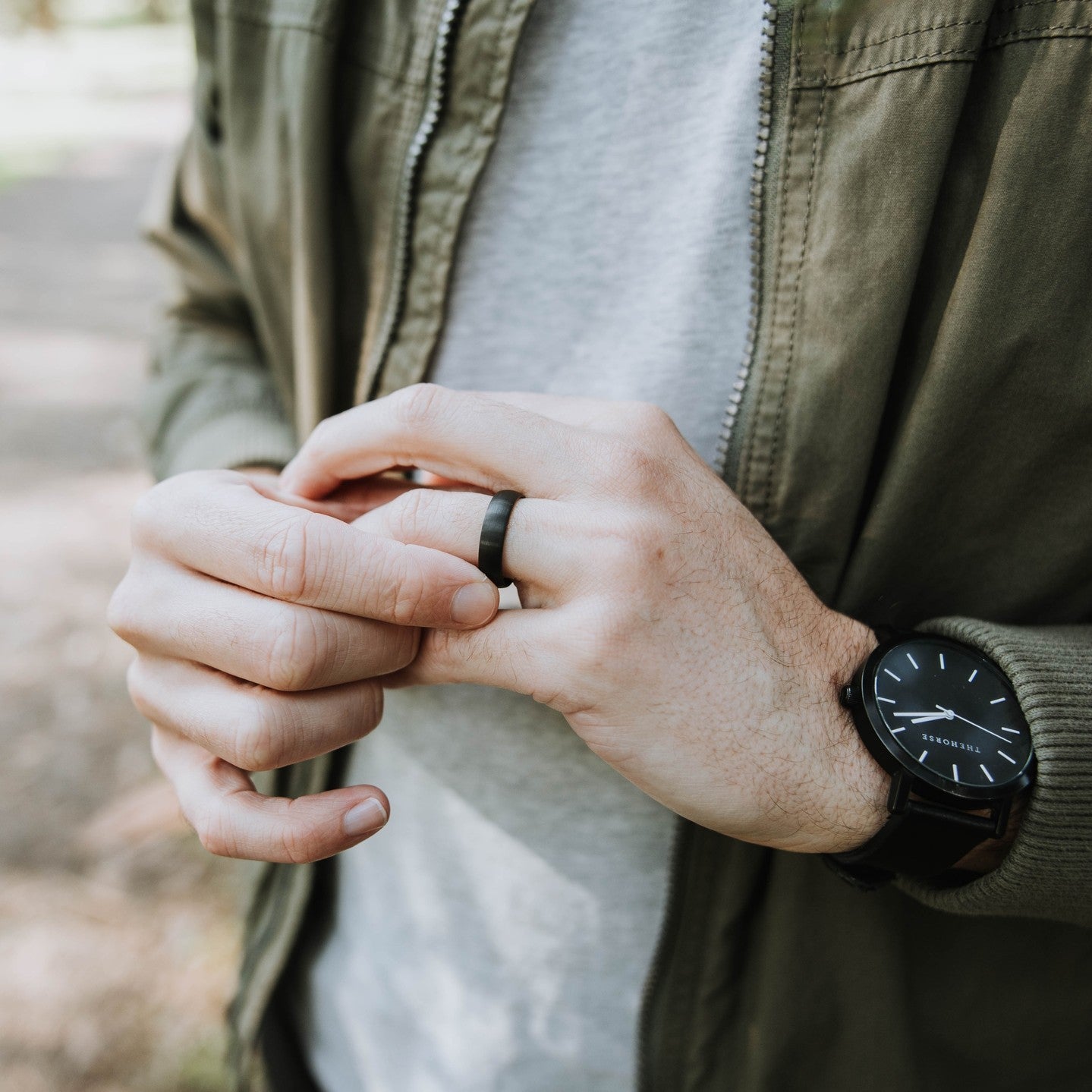 Person wearing a black watch and black wedding ring, with a blurred natural background